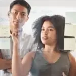 Two colleagues working through notes on a glass board